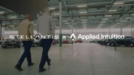 Two people walk through a parking garage, with Stellantis and Applied Intuition brand logos displayed over the top of the image