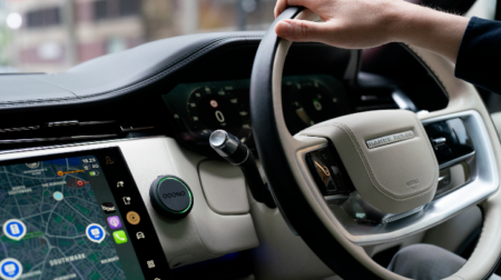 A close up of a driver's hands on the steering wheel and a colourful information display screen
