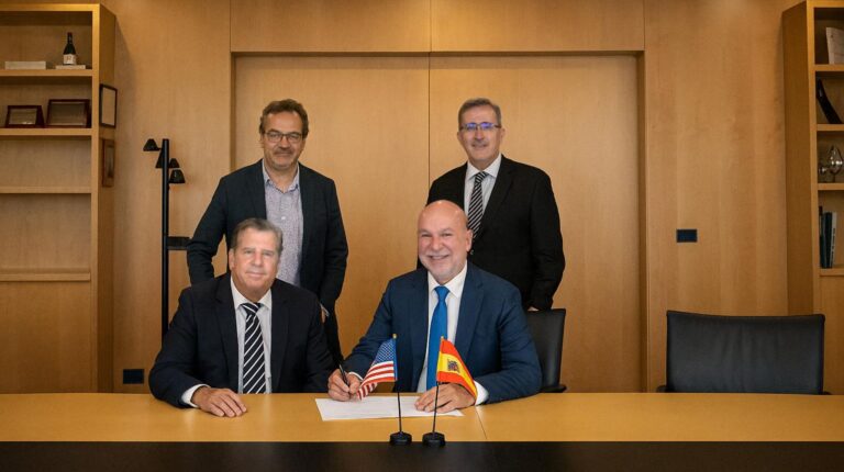 Representatives of Antolin and MAI sit and stand behind a desk in a wood-panelled office to sign the agreement that the companies have signed that produced the speakerless audio system