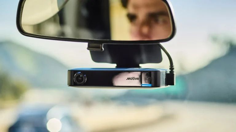 Motive's AI Dashcam Plus positioned below the rearview mirror. The driver's face can be seen in the mirror