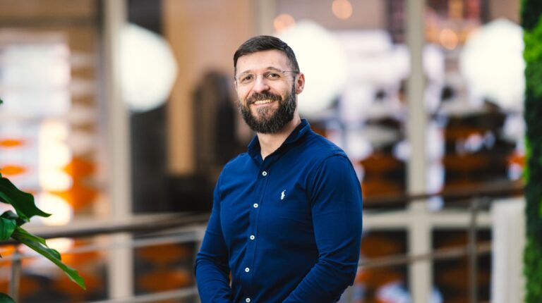 Adrian Capata, senior vice president, Tobii Autosense. He has dark hair and a beard, and is wearing a blue shirt with white buttons while standing in an office.