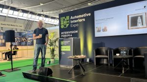 Michael Ries, professor of physics, University of Leeds, stands on the stage at the InteriVision Forum at this week's Automotive Interiors Expo Europe 2026 in Stuttgart, Germany. He is wearing black trousers and t-shirt and is standing in front of a large display screen.