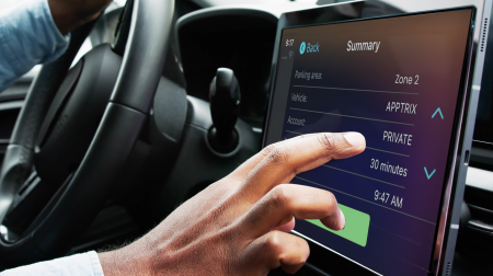 A driver's hand reaches toward the touchscreen in a car.